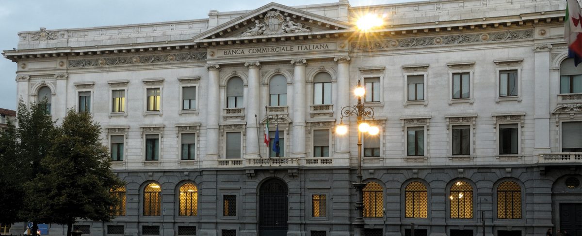 The image of the news that talks about the headquarters of the Gallerie d'Italia in Milan portrays the facade of the building of the Gallerie d'Italia in Piazza Scala in Milan, in a somewhat dark context, with the internal lights on as well as those of the street lamps in the square