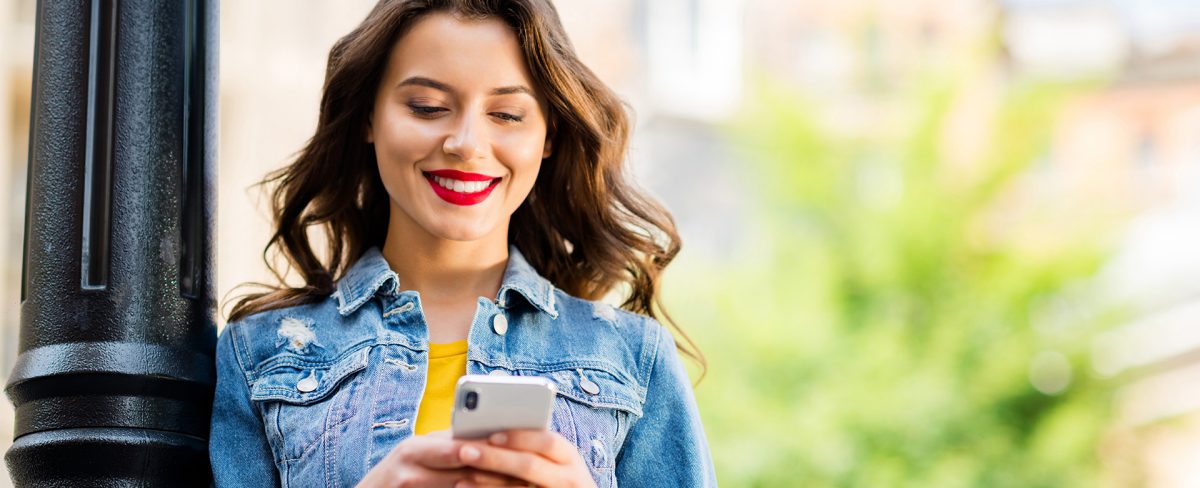 L’immagine che accompagna la News sul report di Forrester Research in cui l’App Intesa Sanpaolo Mobile si conferma “Overall Leader” tra le banking App dell’Area EMEA, ritrae una giovane donna sorridente, con lunghi capelli ondulati, nell'atto di consultare il proprio smartphone in uno spazio aperto, appoggiata al palo di un lampione