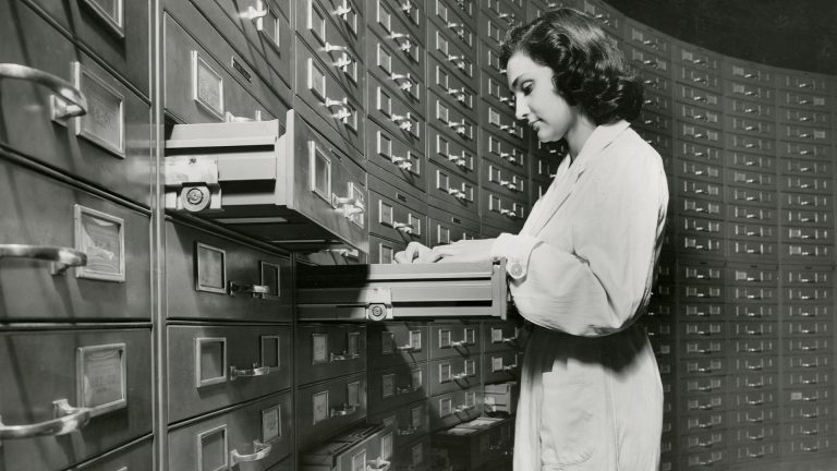 L'immagine ritrae una giovane donna impiegata alla banca Cariplo mentre archivia schede perforate
